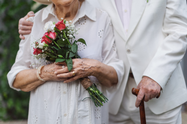 Mid section of senior hands with wedding bouquet and golden wedding rings during their marriage.