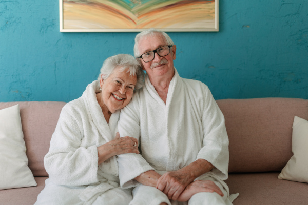 Happy senior couple sitting together in the bathrobe on sofa, having nice time at home.