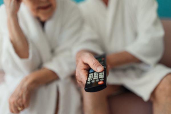 Close-up of senior couple sitting at a sofa in bathrobes and watching TV.