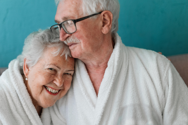 Portrait of happy senior couple sitting together in the bathrobe on sofa, having nice time at home.