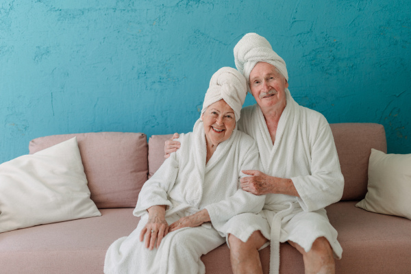 Happy senior couple sitting together in the bathrobe on sofa, having nice time at home.