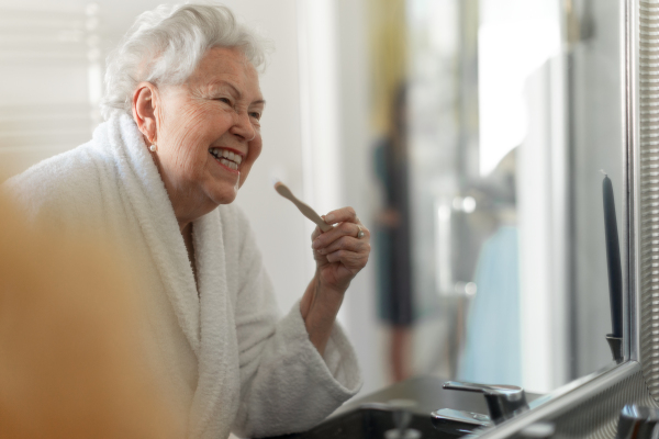 Senior woman cleaning her teeth with a wooden brush in bathroom, sustainable lifestyle.