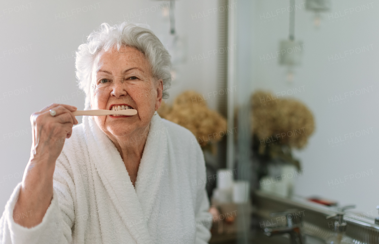 Senior woman cleaning her teeth with a wooden brush in bathroom, sustainable lifestyle.