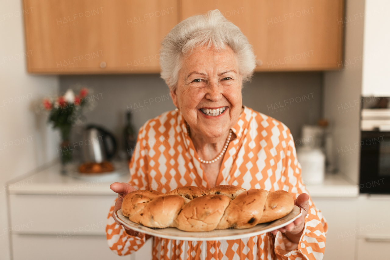 Happy senior woman holding homemade sweet braided bread with raisins.