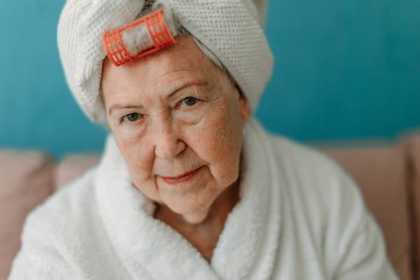 Happy senior woman with a plastic curler sitting at sofa in bathrobes and looking at camera.