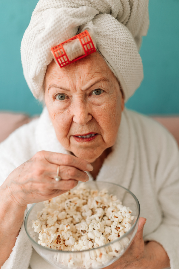 Happy senior couple sitting at a sofa in bathrobes and watching TV with popcorn.