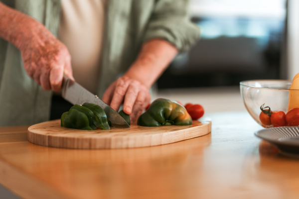 Close-up of a senior man preparing vegetable, cutting at wooden board, healthy lifestyle concept.