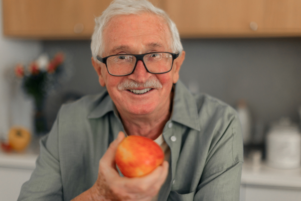 Portrait of senior man holding apples in a kitchen.