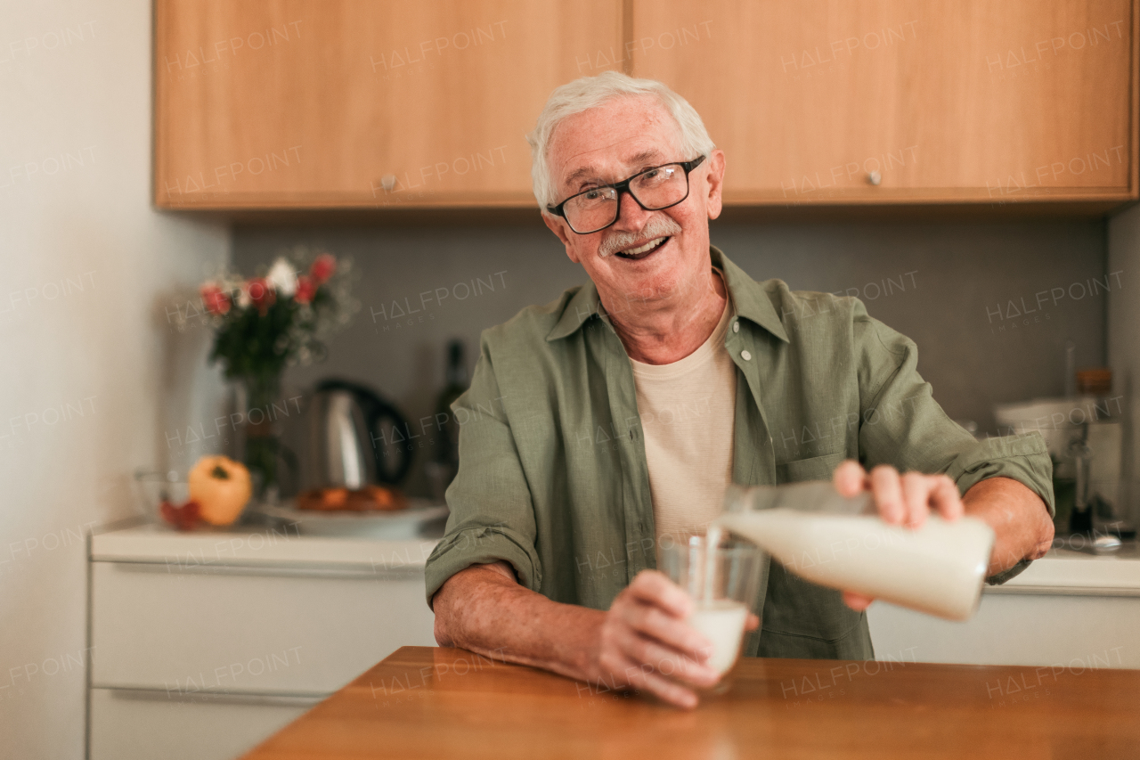 Portrait of senior man sitting in kitchen and pouring milk in a glass. Healthy lifestyle concept.