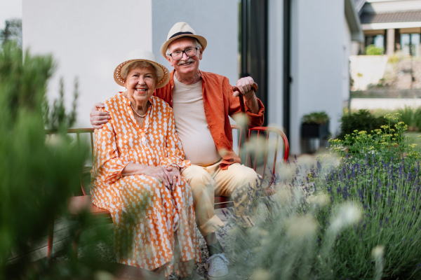 Happy senior couple sitting together in a garden bench, smiling and looking at camera.