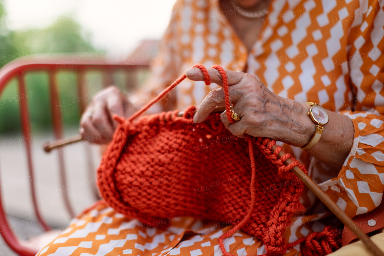 Close-up of senior woman sitting outdoor and knitting scarf.