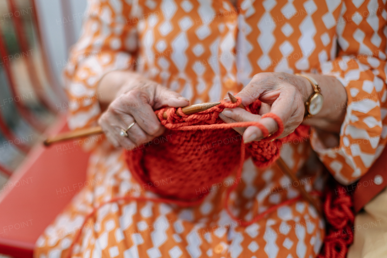 Close-up of senior woman sitting outdoor and knitting scarf.