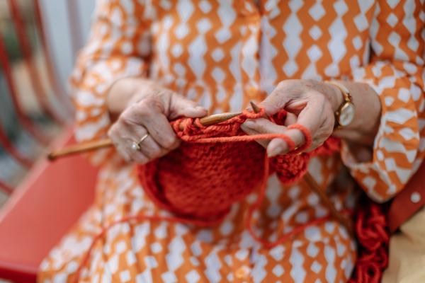 Close-up of senior woman sitting outdoor and knitting scarf.