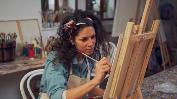 Young artis woman painting at a canvas in her atelier.