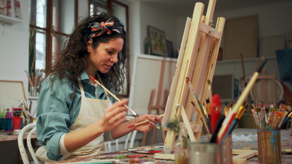 Young artis woman painting at a canvas in her atelier.