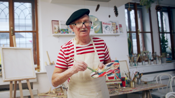 A senior man painting in an artist atelier.