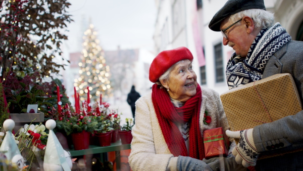 Happy senior couple at outdoor Christmas market, watching and buying a gifts and Christmas decorations.