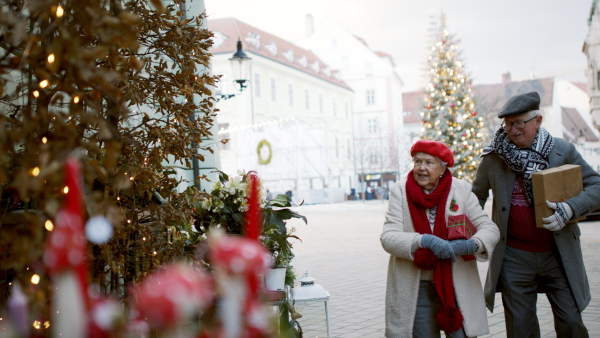 Happy senior couple at outdoor Christmas market, watching and buying a gifts and Christmas decorations.