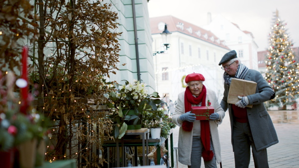 Happy senior couple at outdoor Christmas market, watching and buying a gifts and Christmas decorations.