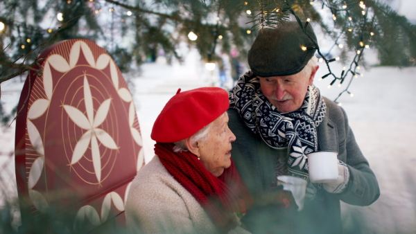 Happy senior couple at outdoor Christmas market, watching and buying a gifts and Christmas decorations.