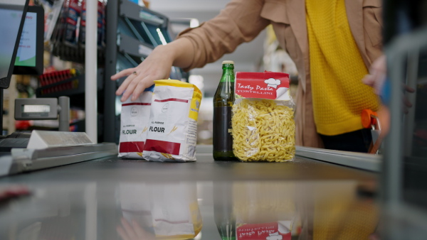 A cropped view of young woman shopping in supermarket, putting products on checking desk