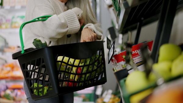 A woman shopping at the supermarket, she is putting vegetables to basket, close-up.