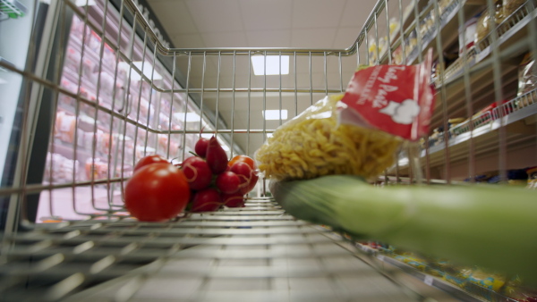 A woman with shopping cart or trolley buying food at grocery store or supermarket, inside view from trolley