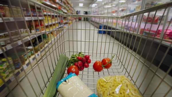 A woman with shopping cart or trolley buying food at grocery store or supermarket, inside view from trolley