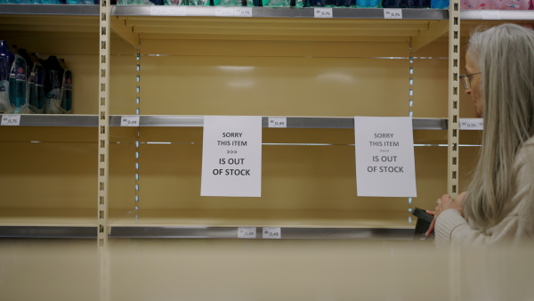 A depressed senior woman shopper in front of empty shelves in a grocery store