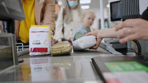 A cropped view of young woman shopping in supermarket, putting products on checking desk