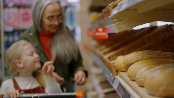 Grandmother with her granddaughter choosing and buying bread in supermarket.