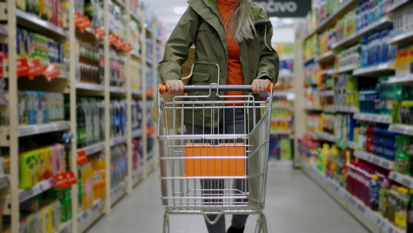 An elder woman walking with empty trolley and shopping in supermarket, inflation and increasing prices concept.