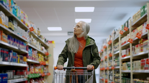 An elder woman walking with empty trolley and shopping in supermarket, inflation and increasing prices concept.