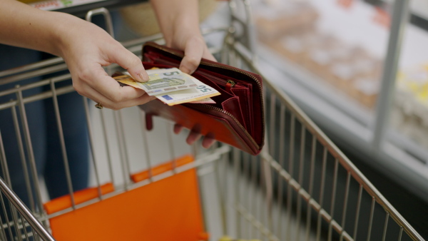 A worried woman checking her wallet when shopping in supermarket. Inflation and economic recession concept.