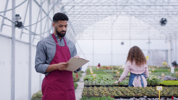 Young colleagues working in garden centre, man with clipboard.