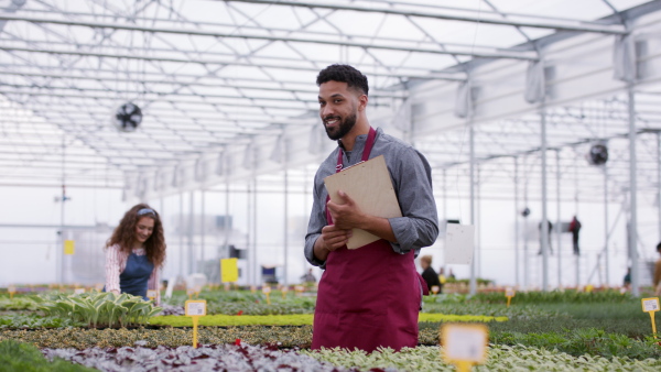 Young colleagues working in garden centre, man with clipboard looking at camera.