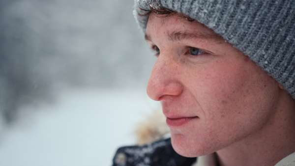 A close-up of young man in winter under falling snow in nature.