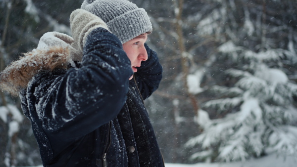 A young man in winter under falling snow in nature.