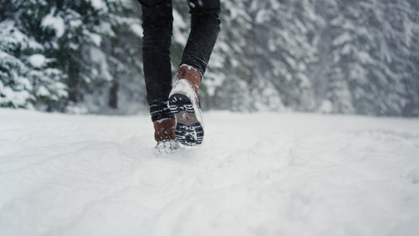 A low-section of unrecognizable man in winter boots walking along snowy path in wintery nature