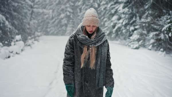 An unhappy young woman standing and breathing fresh air in the snowy nature.