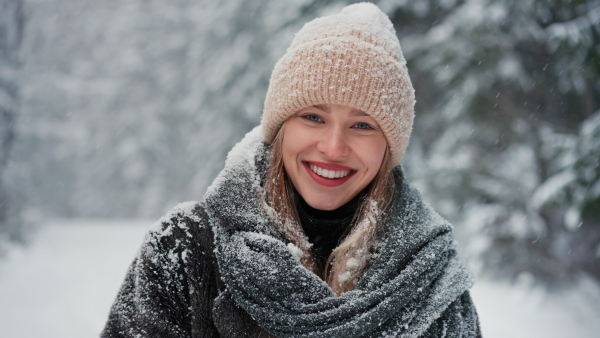 A happy young woman in winter under falling snow in nature looking at camera