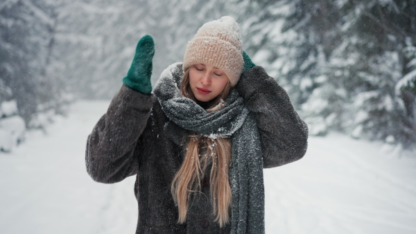 A happy young woman in winter under falling snow in nature looking at camera