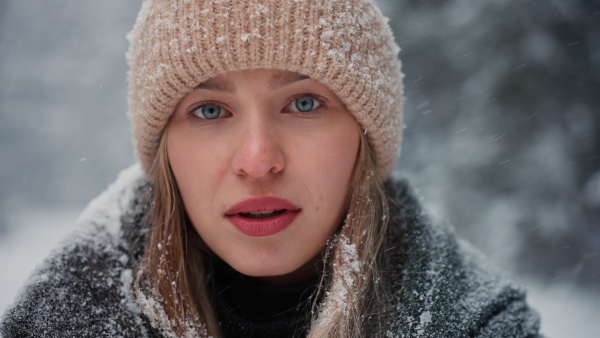 A happy young woman in winter under falling snow in nature looking at camera