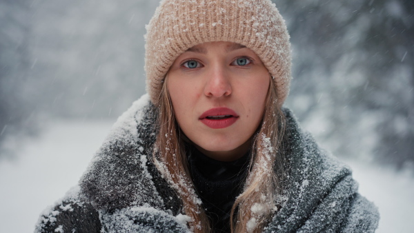 Close up of an unhappy young woman standing and breathing fresh air in the snowy nature.