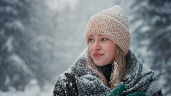 A happy young woman in winter under falling snow in nature looking at camera