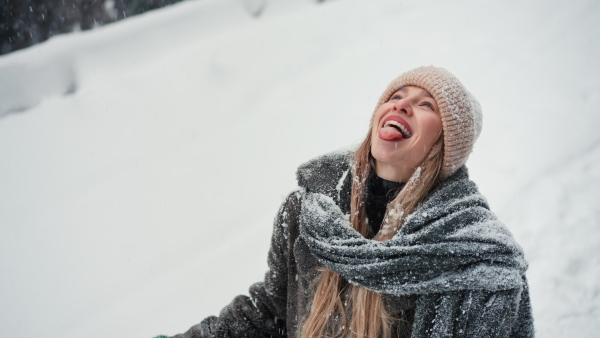 A happy young woman in winter under falling snow in nature catching snowlakes at her tongue.