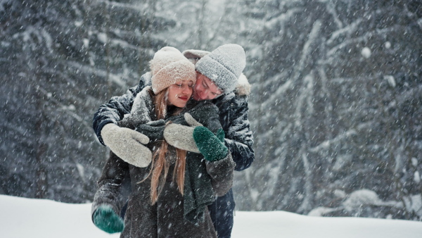 A young couple hugging and kissing in winter under falling snow in nature.