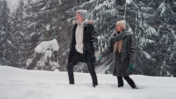 A happy young couple in love walking in wintery nature under falling snow.