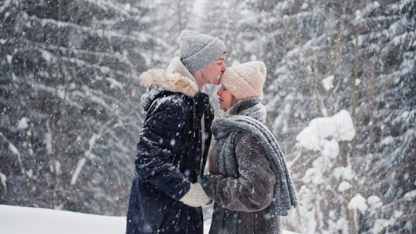 A close-up of young couple hugging and kissing in winter under falling snow in nature.