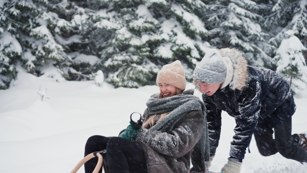 A young couple in love sledding in wintery nature under falling snow.